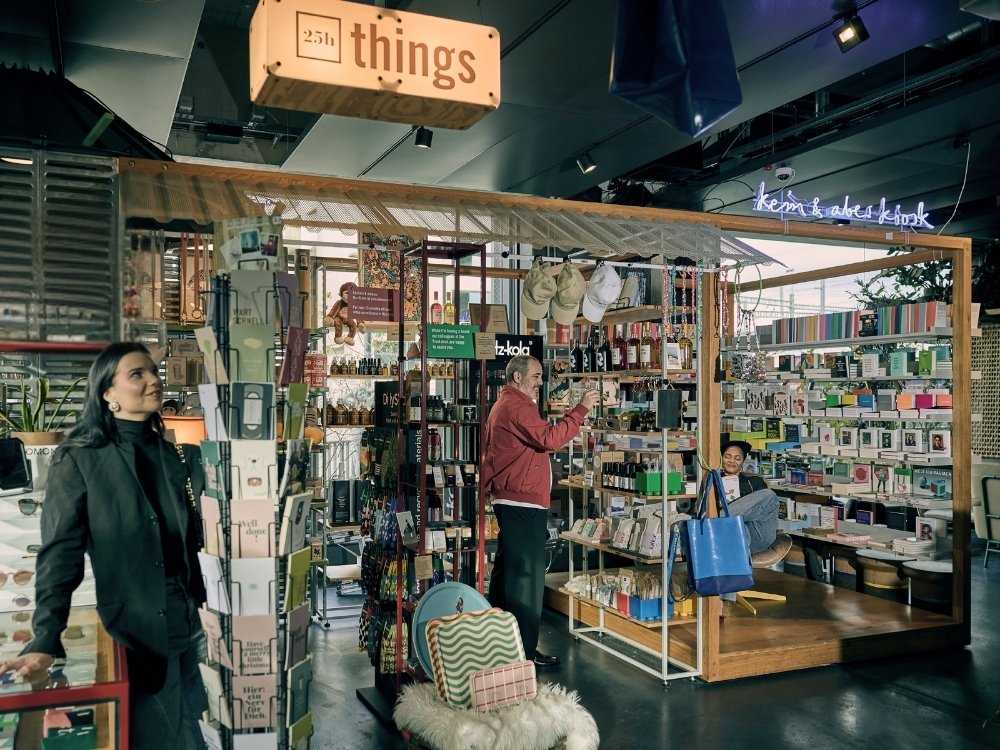 People browsing and sitting in a modern store section labeled "things," featuring books, bottles, cards, and various small items.