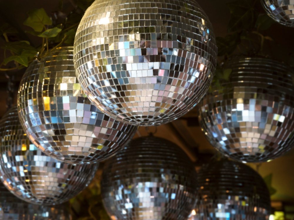 A cluster of shimmering disco balls hanging from the ceiling, reflecting light with colorful mosaic patterns.