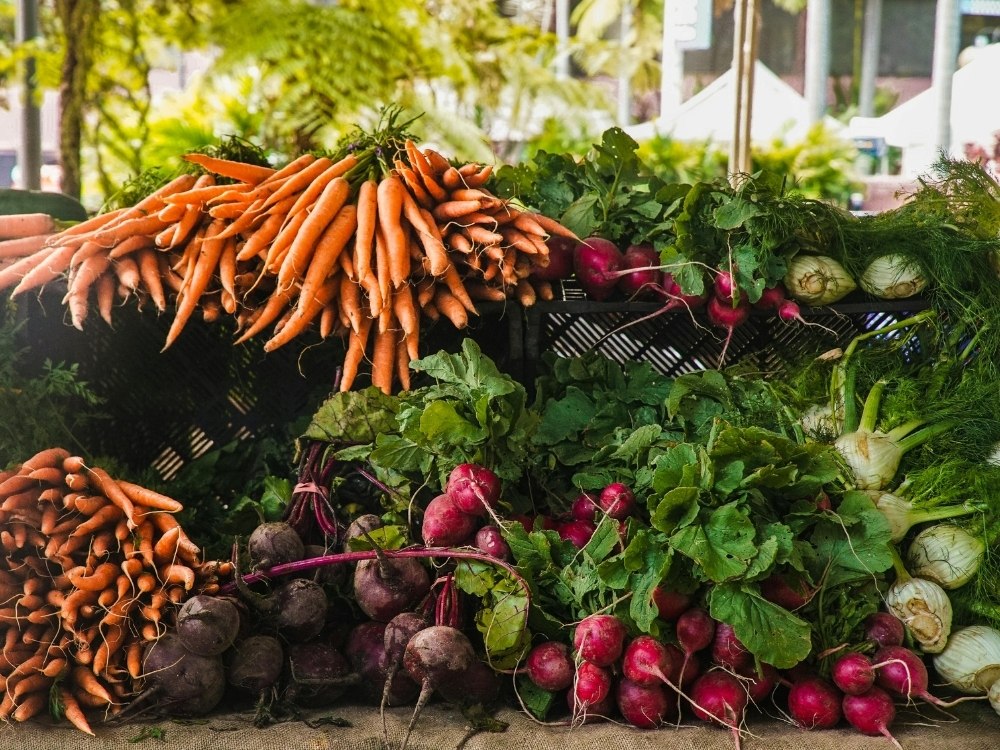 A vibrant display of fresh vegetables, including orange carrots, purple beets, and various leafy greens, arranged on a market stall.