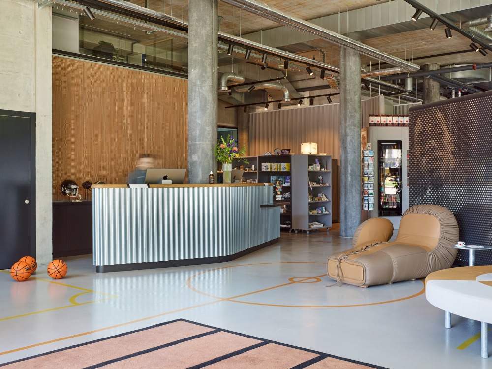 Reception area with a corrugated desk, decorative plants, sports memorabilia, and casual seating, featuring basketballs on the floor.
