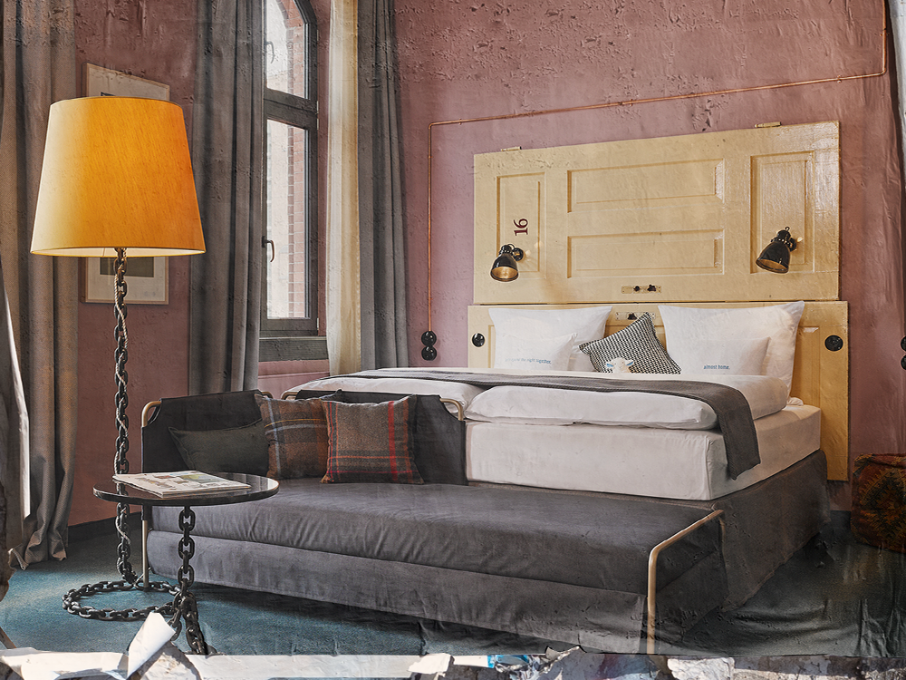 Stylish hotel room featuring a yellow headboard, plush bedding, a cozy sofa, a patterned pillow, and a standing lamp beside large windows.