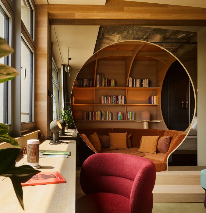Reading nook featuring a circular wooden shelf filled with books, a plush sofa, desk, and modern decor in a stylish interior.