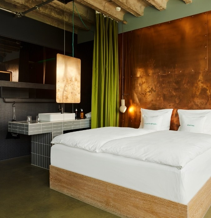 Modern hotel room featuring a minimalist design with a wooden bed, green curtains, a copper wall, and elegant lighting.