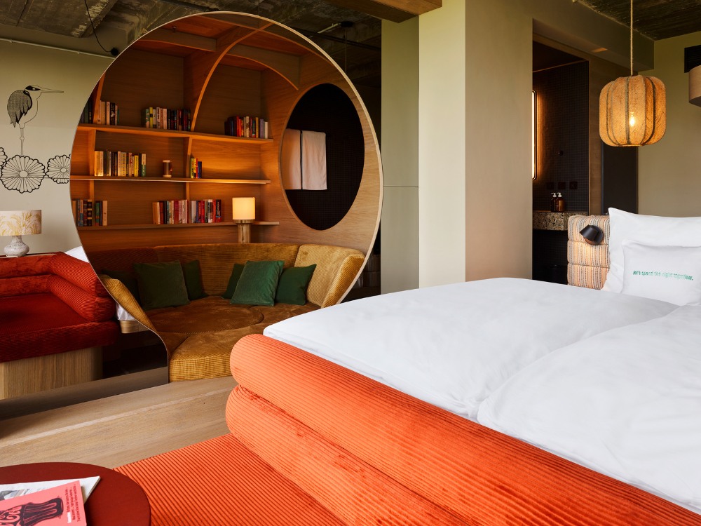 Hotel room featuring white bedding, a circular nook with bookshelves, and a cosy seating area. Warm lighting and artistic decor create a relaxed ambience.