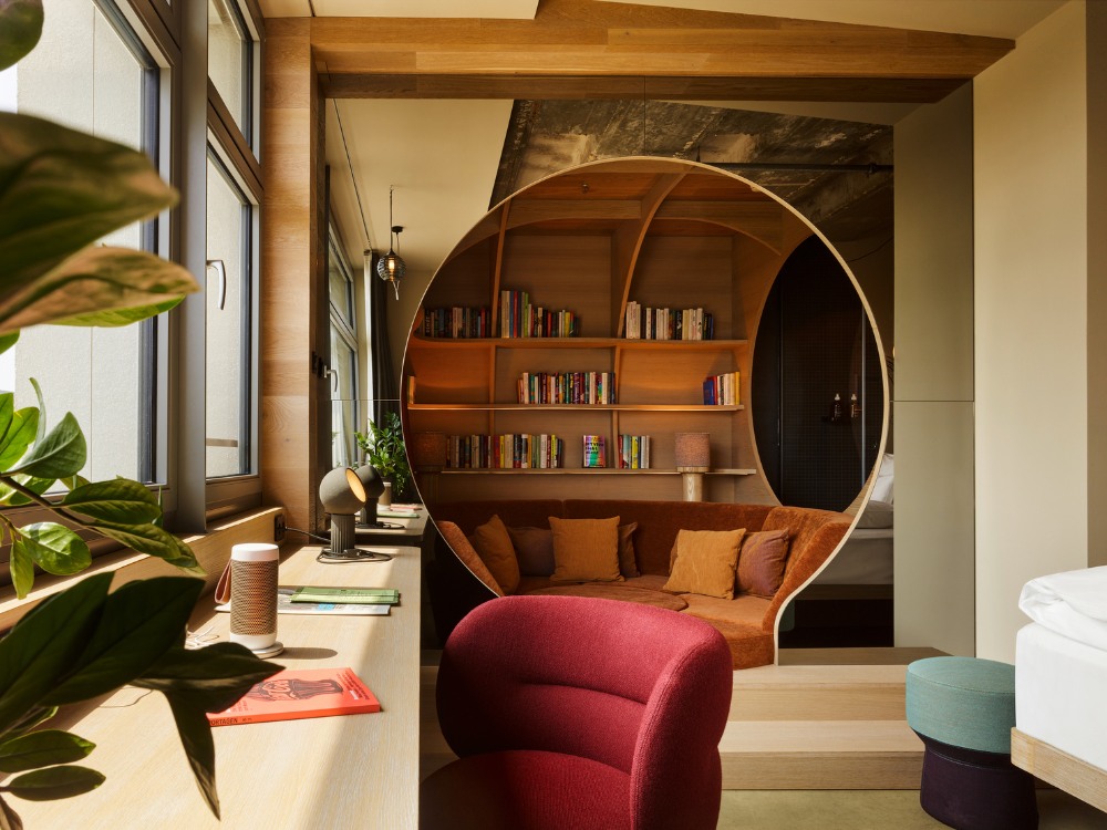 Modern reading nook with circular bookshelf, cosy rust-colored seating, and warm lighting. Plants and books add a calm, inviting atmosphere.