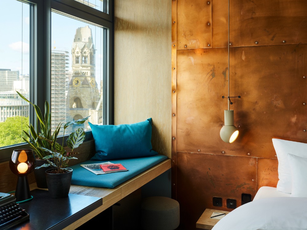 Hotel room with a copper wall, a blue cushion seat by the window, and a view of the Memorial Church in Berlin.