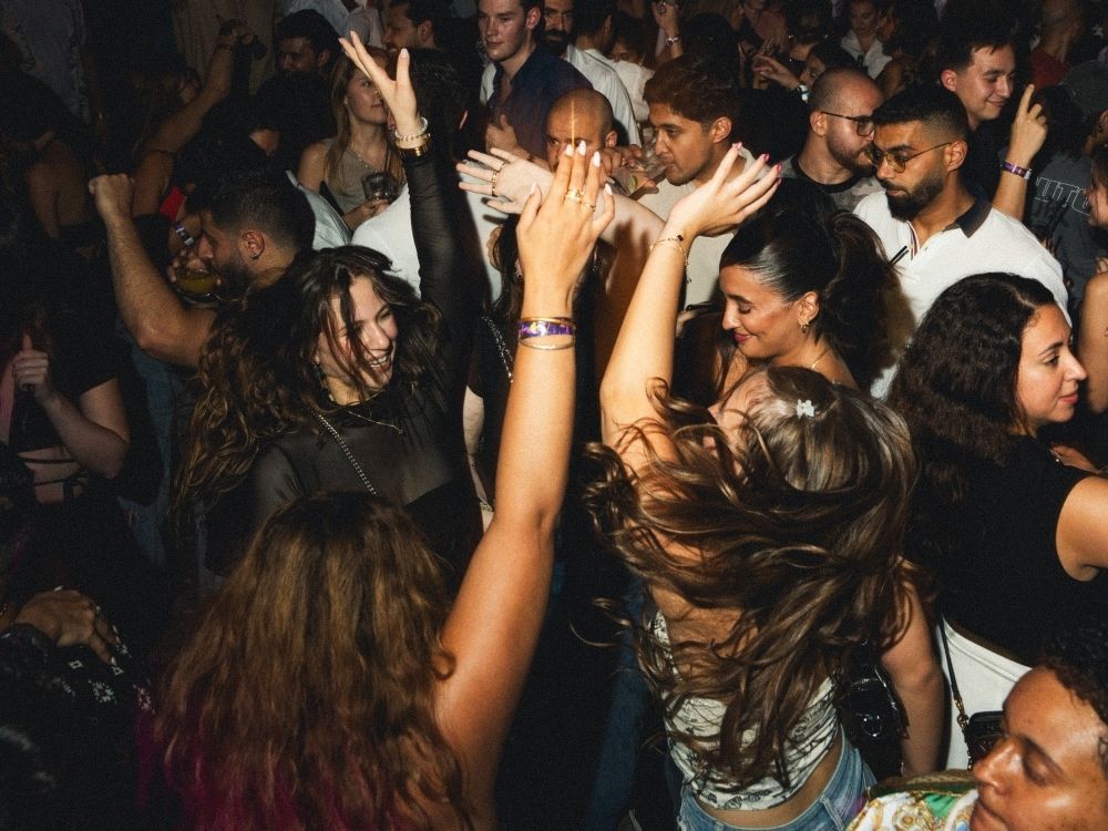 A lively crowd dances with raised arms in a vibrant party atmosphere, showcasing excitement and energy on the dance floor.