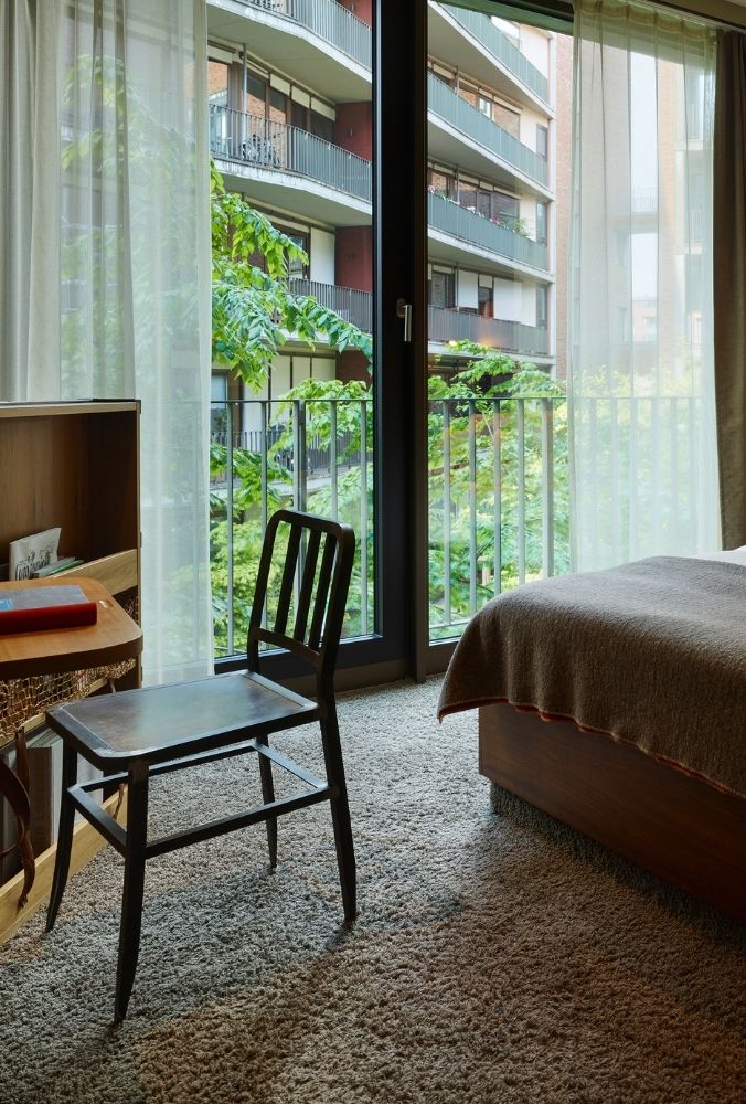 Modern hotel room featuring a double bed, wooden accents, and large Windows. Cosy and stylish decor.