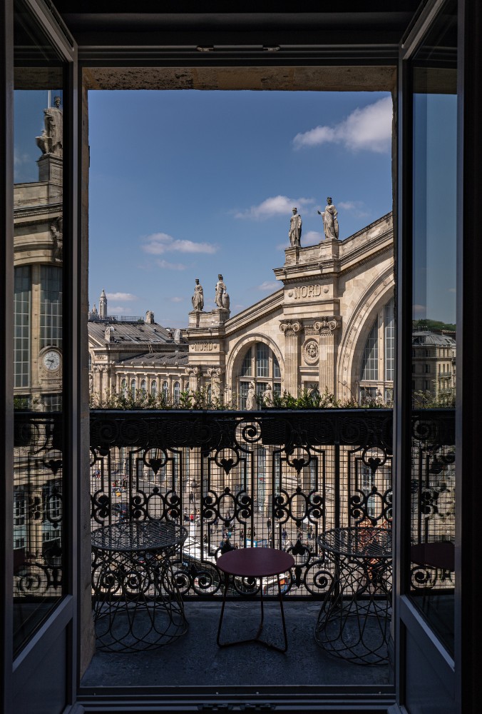 View from a balcony featuring ornate railings, overlooking historical architecture and a bustling street under a blue sky.