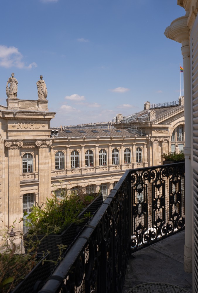 View of the ornate rooftop of Gare du Nord in Paris, framed by wrought iron balcony railings under a clear blue sky.