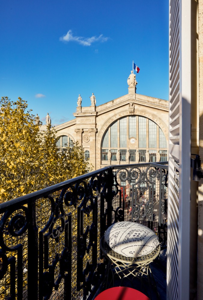 View from a balcony overlooking a historic train station with a French flag, surrounded by autumn foliage under a clear blue sky.