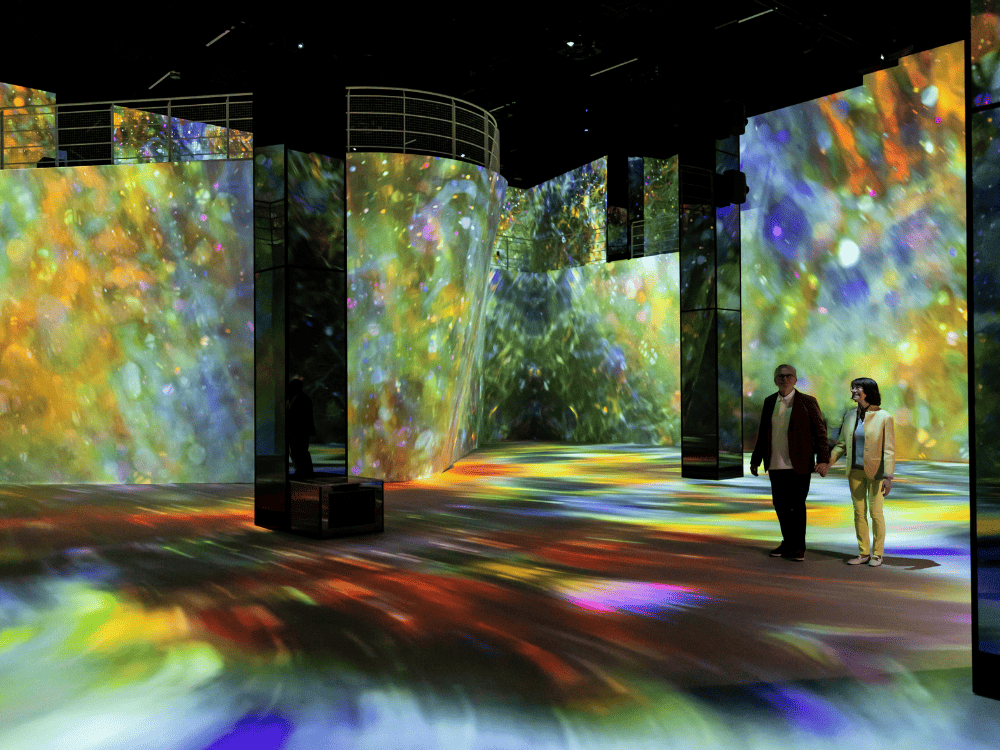 Visitors explore an immersive art space filled with vibrant, colorful projections creating a dynamic atmosphere.