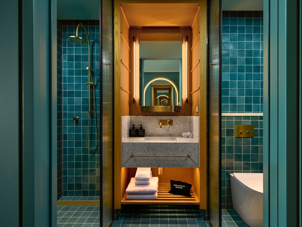 A modern bathroom featuring teal tiles, a sleek marble sink, golden fixtures, and a circular mirror reflecting stylish details.
