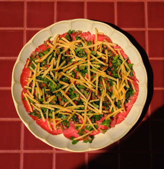 A vibrant salad featuring layers of tomatoes, chopped greens, and crispy fried strips, presented in a beige plate.