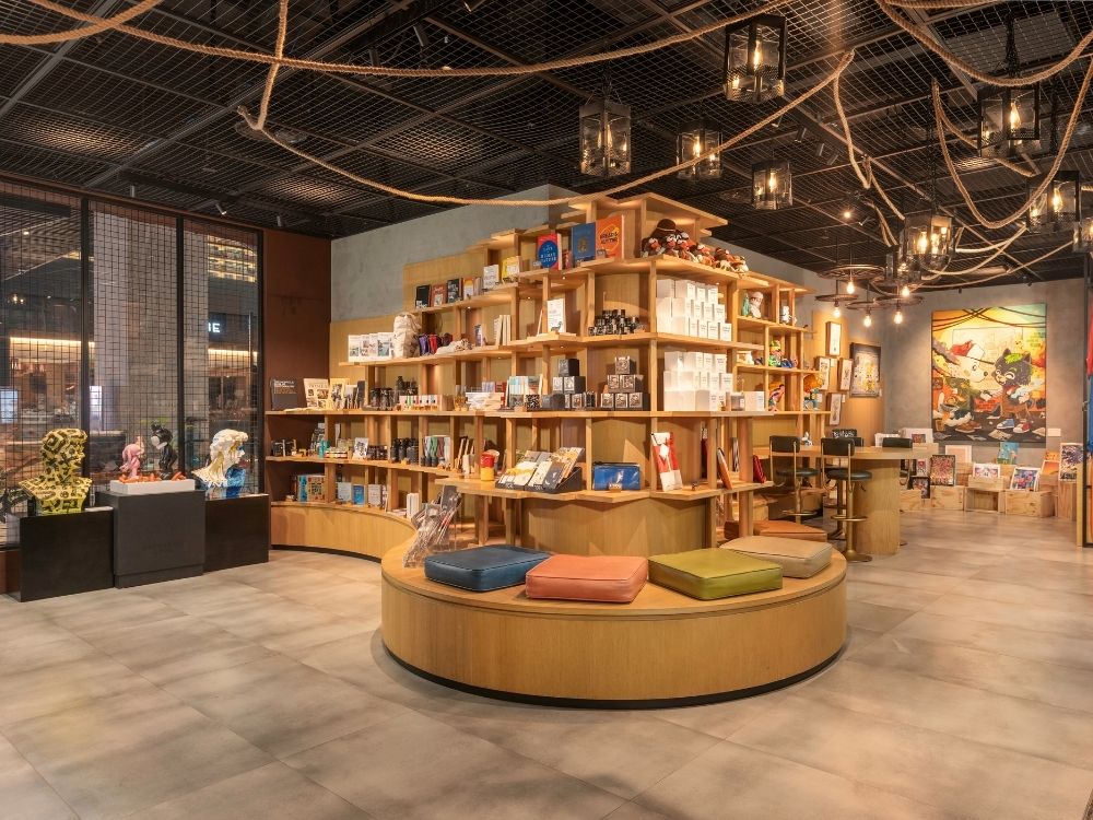 Modern hotel lobyb interior with warm lighting, featuring circular wooden shelves filled with books and decor. Colorful cushions on benches create a cosy atmosphere.