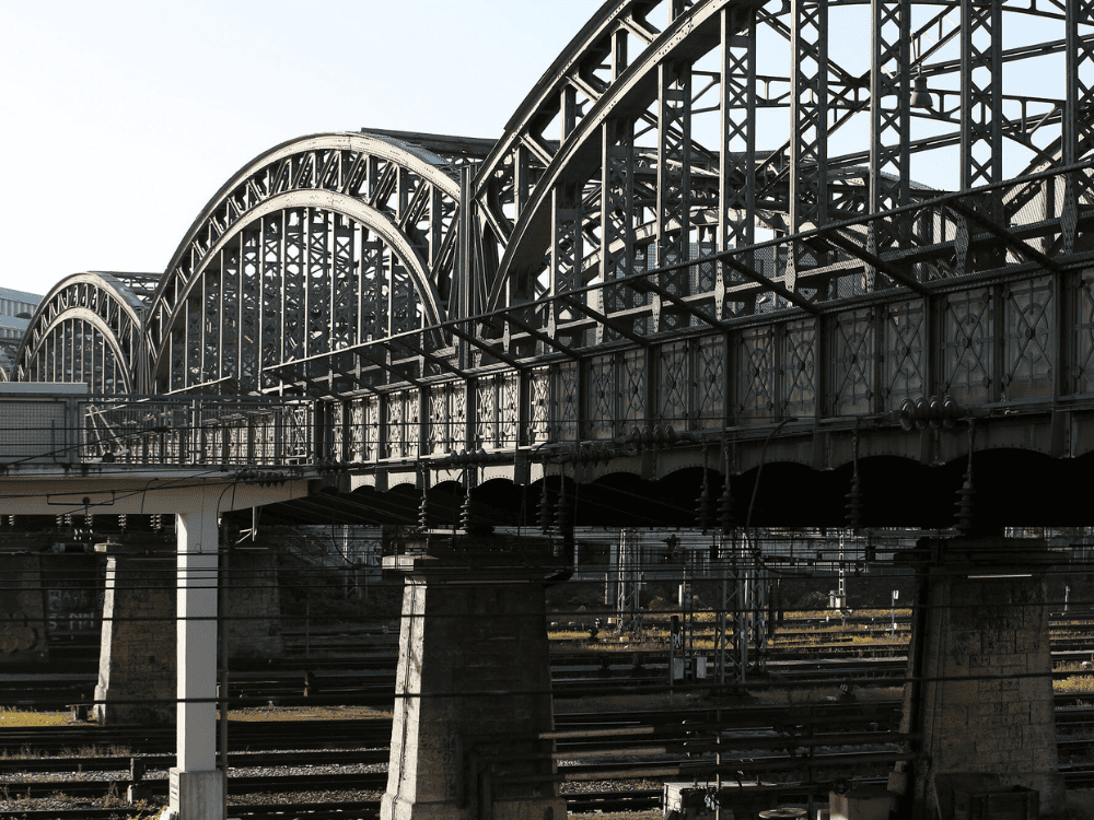 Steel railway bridge with multiple arches and intricate lattice design, spanning over train tracks.