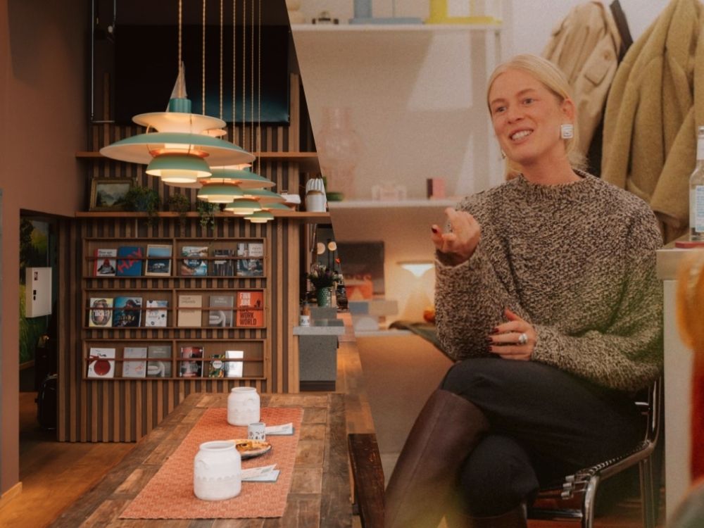 A woman speaks and gestures during a small workshop in a cosy café setting, with warm lighting, shelves of books and a wooden table in the foreground