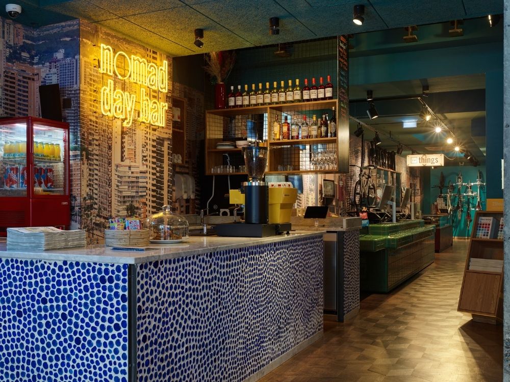 Brightly lit bar with a blue mosaic countertop, neon signage, and a variety of drinks displayed on shelves in a modern interior.