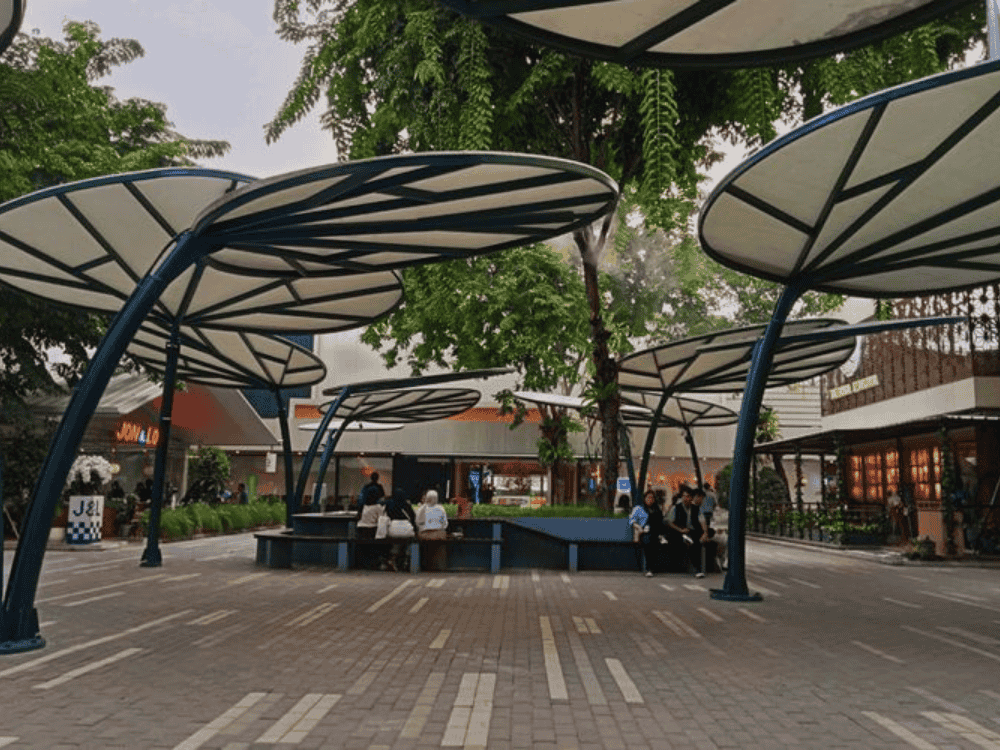Modern outdoor space with large, leaf-like canopies providing shelter for people sitting on benches.