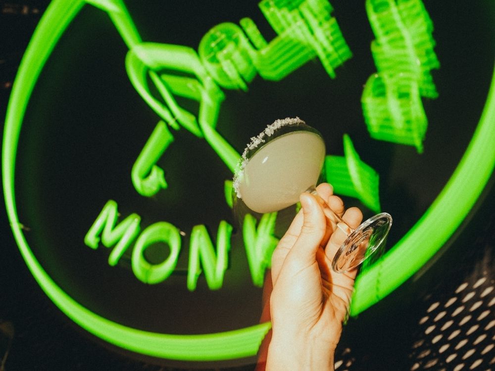 Hand holding up a cocktail glass in front of the Monkey Bar logo.