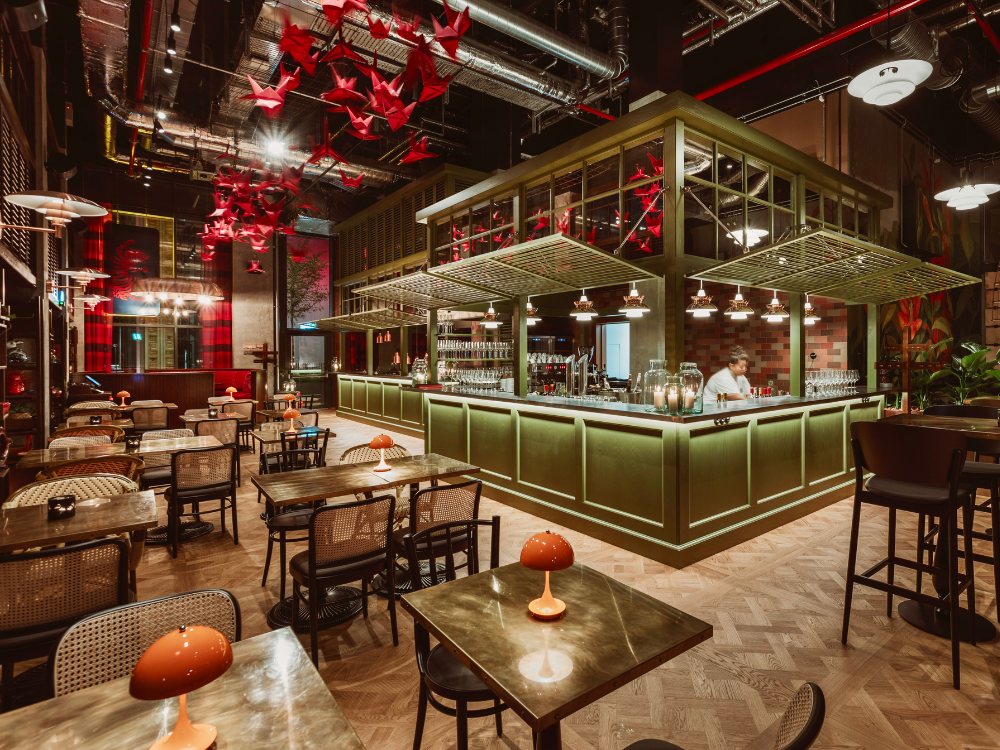 Chic restaurant interior featuring green bar, wooden tables, modern lighting, and red paper cranes suspended from the ceiling.