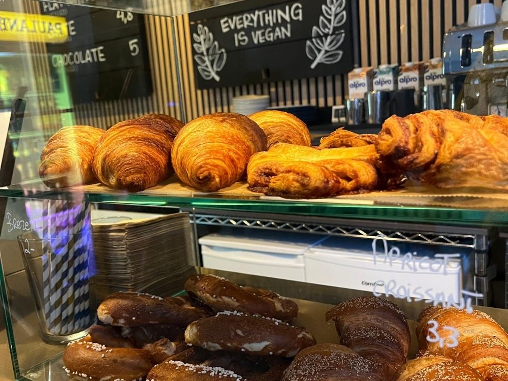 A display case with vegan pastries, including croissants and pretzels. A chalkboard above reads "Everything is vegan" with decorative leaves.