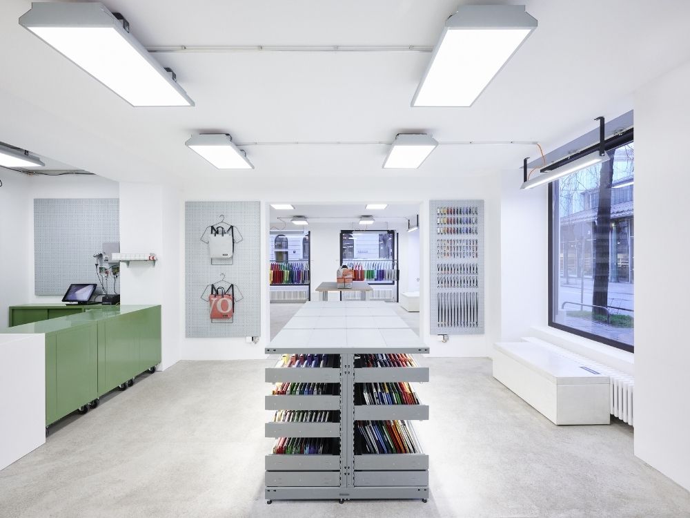 Modern retail space with bright lighting, featuring colorful items on display, a green checkout counter, and large windows for natural light.