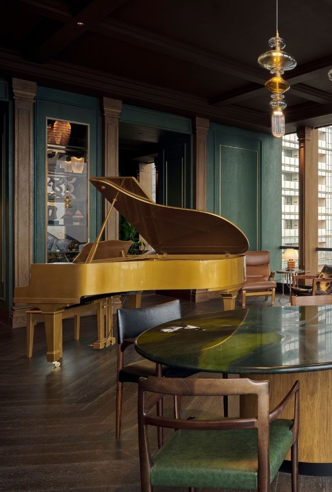 Elegant room with a golden grand piano, dark wood accents, green walls, and modern pendant lights, creating a luxurious and sophisticated ambiance.