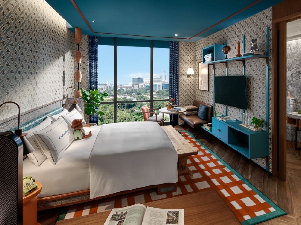 Stylish hotel room with a patterned carpet, large bed, and cityscape view through floor-to-ceiling windows.