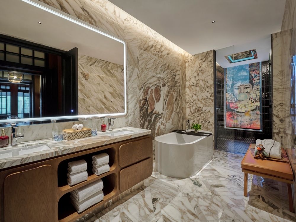Luxurious bathroom with marble walls and floor, featuring a modern bathtub, double sink vanity with mirror, and colorful artwork near a glass shower.