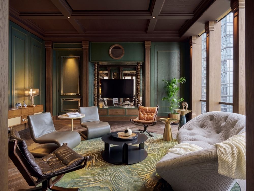 Luxurious living room with wood paneling and green accents. Modern chairs, round coffee tables, plush sofa, and warm lighting create an inviting, elegant atmosphere.
