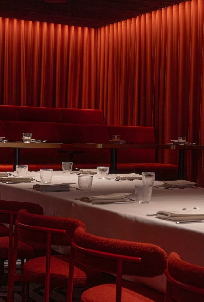 Red-themed restaurant interior with soft lighting and red velvet curtains. White tablecloths on tables, set with glasses and napkins.