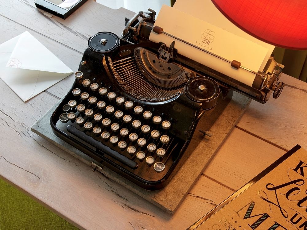 Vintage black typewriter on a wooden desk with a letter, paper in the carriage, and a red lamp nearby.