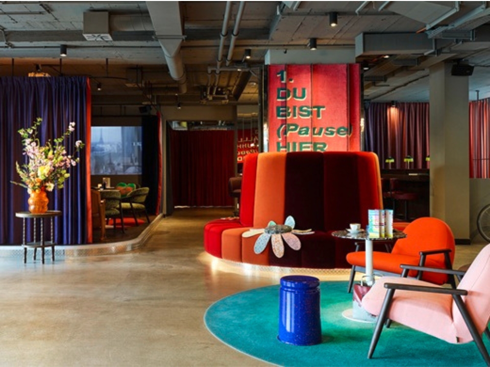 Stylish, modern room with colorful seating and decor. Features include a round red couch, vibrant pink and orange chairs, blue rug, and flowers.