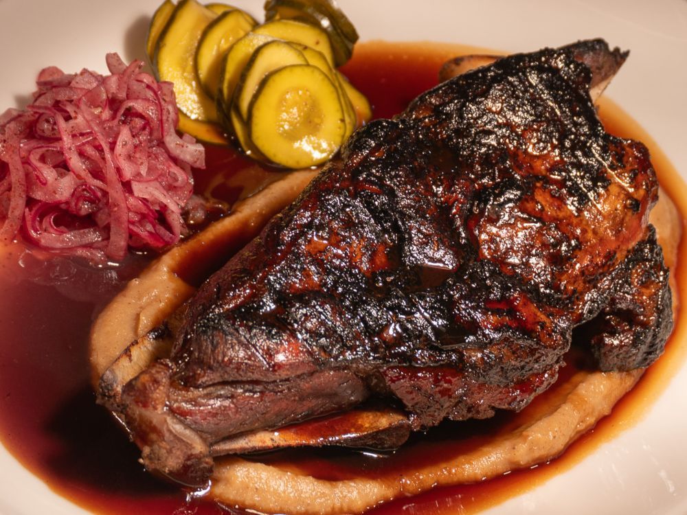 Grilled steak served with sliced pickles, pickled red onions, and a rich brown sauce on a white plate.
