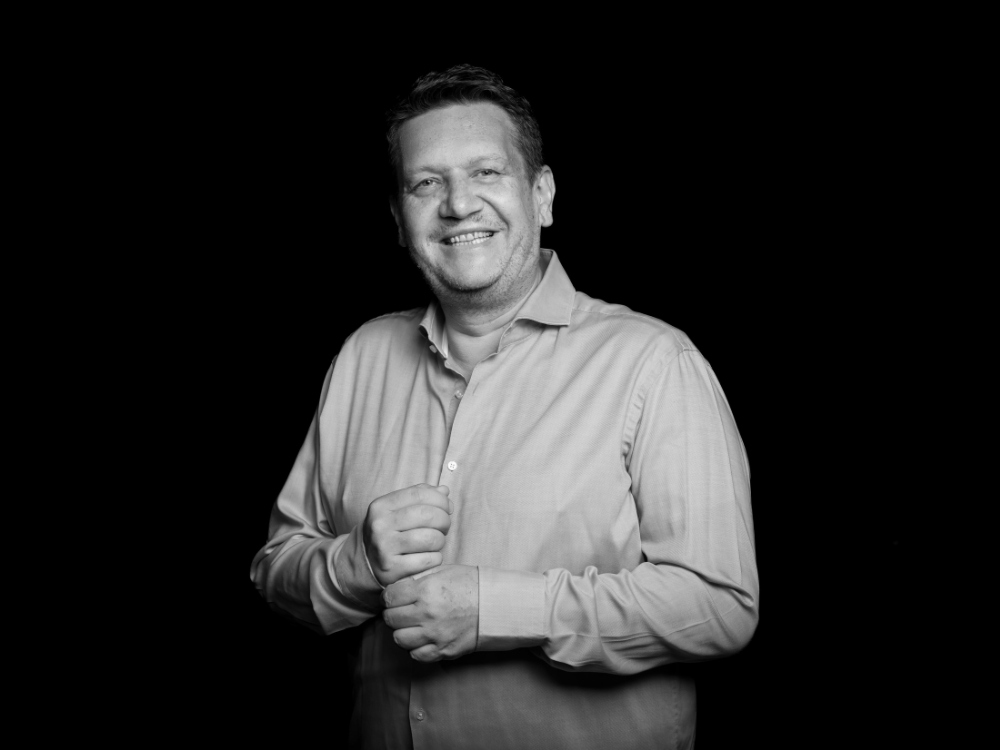 Black and white photo of a person in a long-sleeve button-up shirt adjusting their cuff against a dark background.