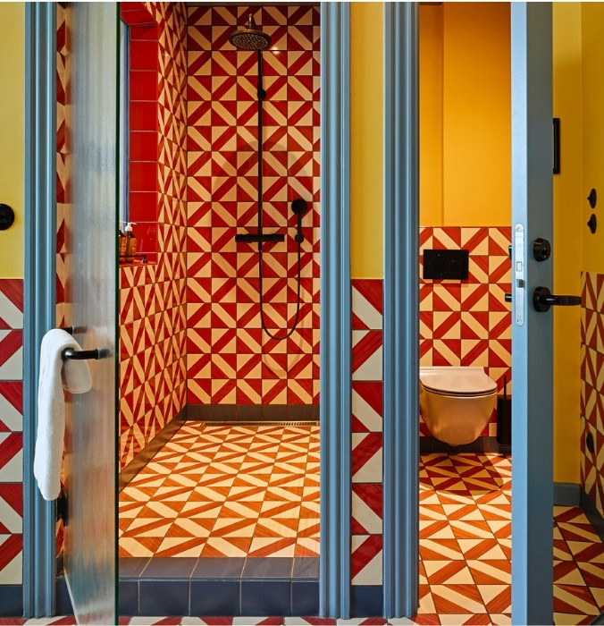 Vibrant hotel bathroom showcasing a walk-in shower and toilet area fully tiled in eye-catching red and white geometric patterns.