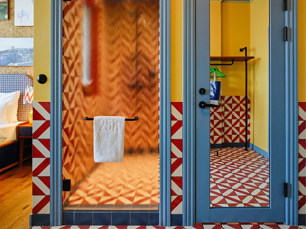 A frosted glass shower door with a white towel reflecting bold red and white geometric triangular tiled walls and blue framing.