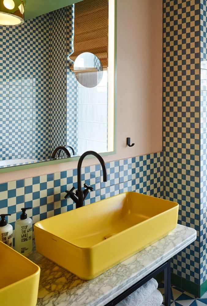 Close-up of a bright yellow rectangular vessel sink on a white marble vanity counter against a blue-and-white checkered tiled wall in a boutique hotel.