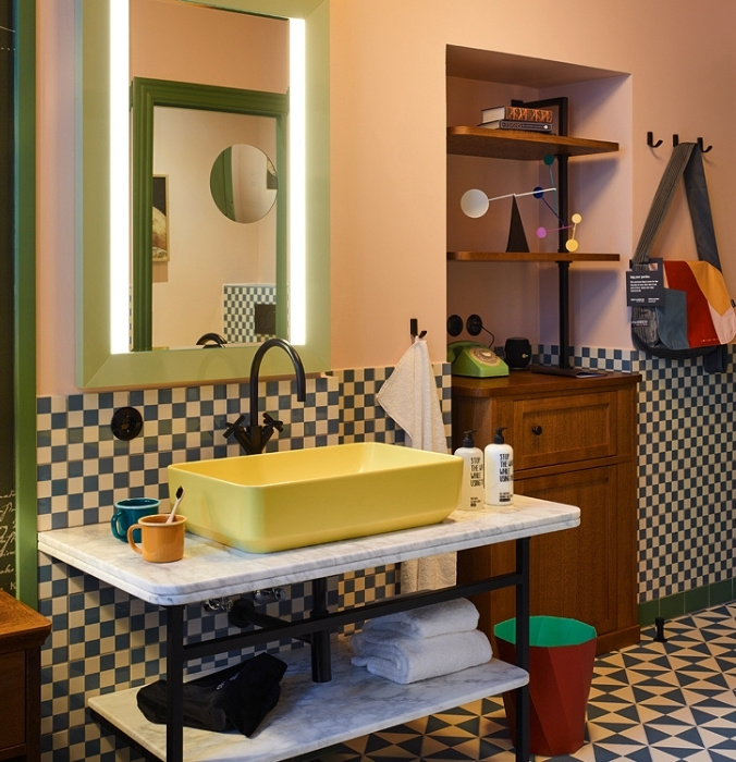 Retro hotel bathroom featuring a bright yellow rectangular vessel sink on a marble-top vanity table, blue-and-white checkered tiled walls, and a green-framed mirror.