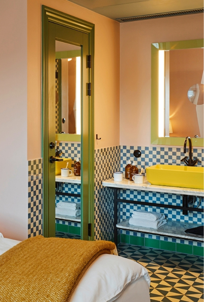 Stylish hotel vanity station featuring a bright yellow vessel sink on marble, a green door frame, and blue-and-white checkered tiled walls.