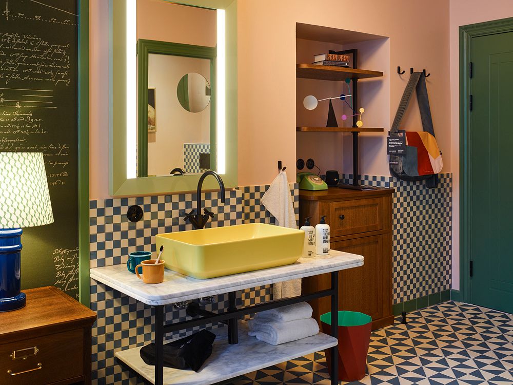 Eclectic hotel guest room with a green door and chalkboard wall looking through to an open-concept washroom featuring a bright yellow vessel sink.