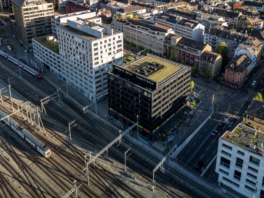 Aerial view of a bustling city with a train track weaving through buildings and green spaces.