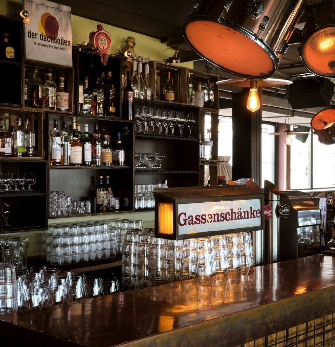 A well-stocked bar counter displaying an assortment of colorful bottles and glassware.