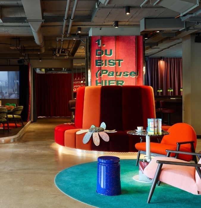 A vibrant lobby featuring a large round couch surrounded by colorful chairs, creating an inviting seating area.