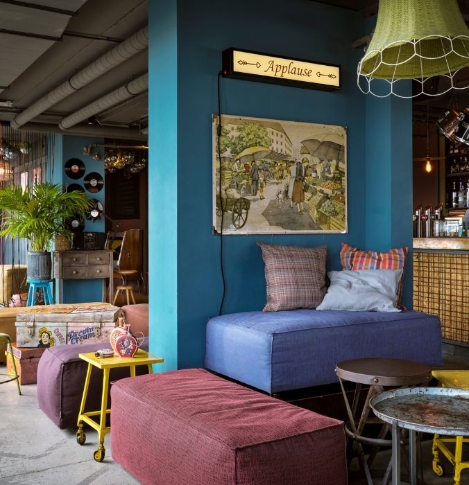 A lively bar adorned with a big, colorful painting, bright decor, and comfortable seating for a cheerful vibe.