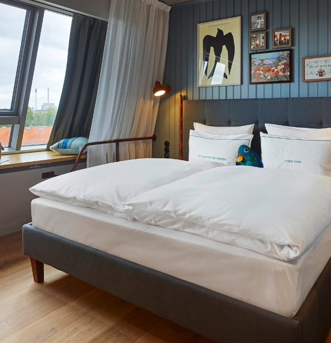 Modern guest bedroom featuring blue vertical wood-paneled walls, framed graphic prints, a plush bed with white linens, and a slanted attic window.