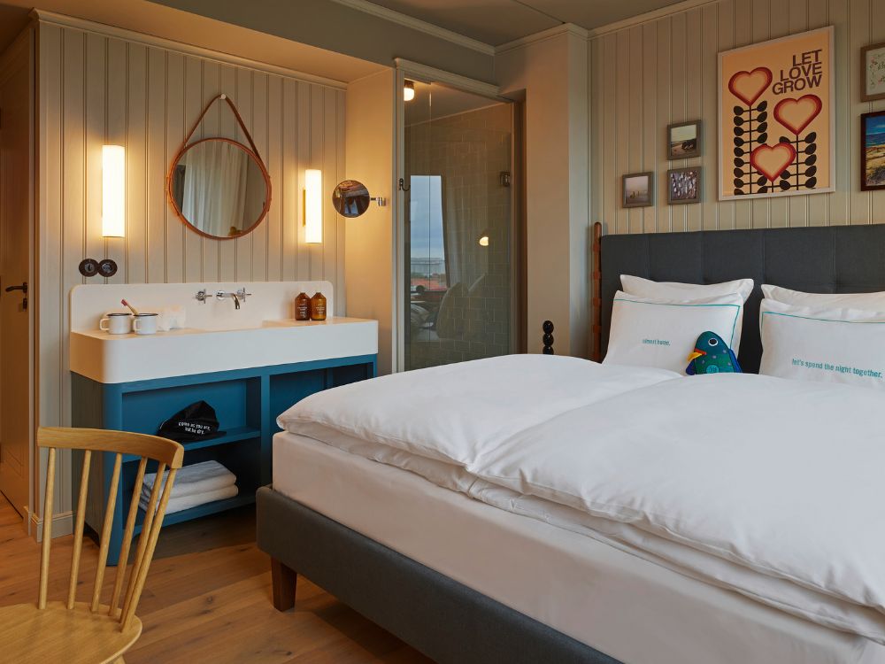 Boutique hotel bedroom layout showcasing a king-size bed on hardwood floors next to an integrated washbasin vanity with a blue cabinet and glass shower.