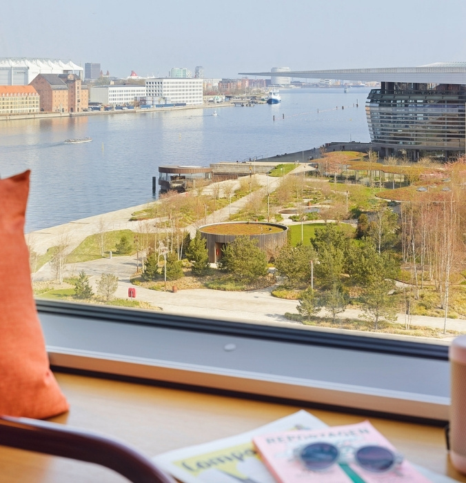 Scenic waterfront view from a hotel window overlooking the Royal Danish Opera House, harbor canal, and green landscaped park in Copenhagen.