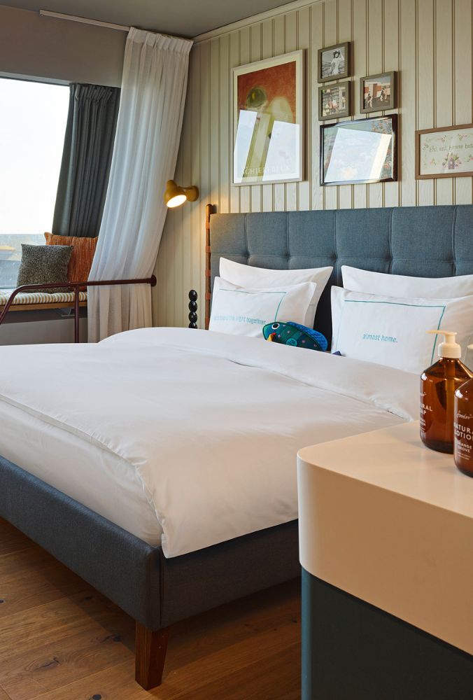 Comfortable double bed with a grey button-tufted headboard next to a window seat, looking past an open-concept white vanity counter.